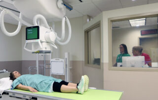 Person in x-ray room receiving an x-ray; x-ray techs are seen in the background